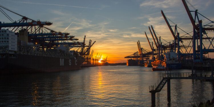 Shipping vessels at Hamburg port during a vibrant sunset, showcasing industrial cranes.