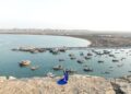 An aerial view of Chabahar harbor with numerous boats and a couple standing on a rock.