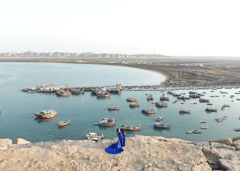 An aerial view of Chabahar harbor with numerous boats and a couple standing on a rock.