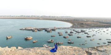 An aerial view of Chabahar harbor with numerous boats and a couple standing on a rock.