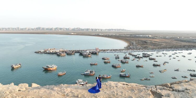 An aerial view of Chabahar harbor with numerous boats and a couple standing on a rock.