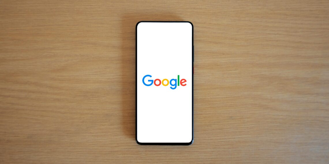 A smartphone displaying the Google homepage on a wooden surface, viewed from above.