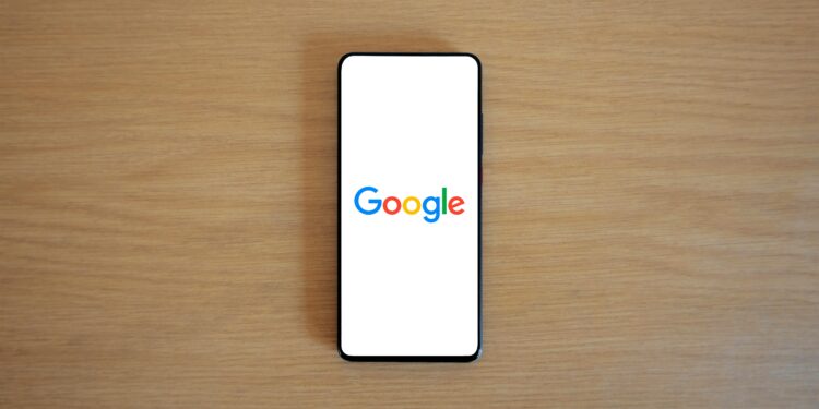 A smartphone displaying the Google homepage on a wooden surface, viewed from above.