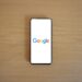 A smartphone displaying the Google homepage on a wooden surface, viewed from above.